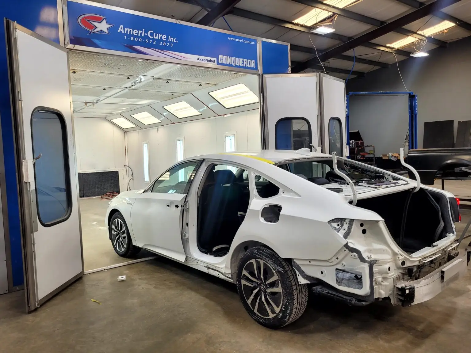 A damaged car prepped for collision repair and painting outside a professional spray booth.